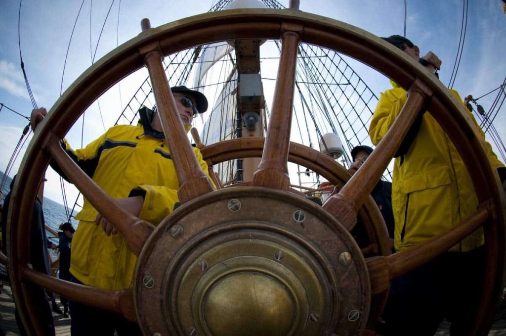 Two men captain the helm of this large vessel with a massive steering wheel.