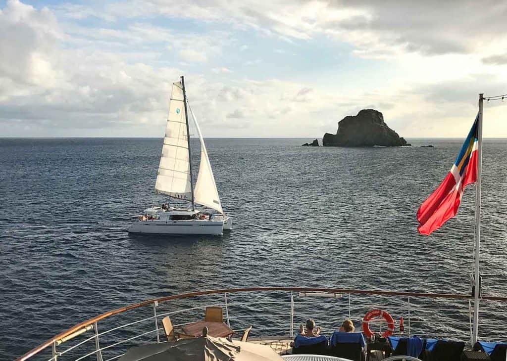 A catamaran is shown sailing past a cruise ship in this photo.