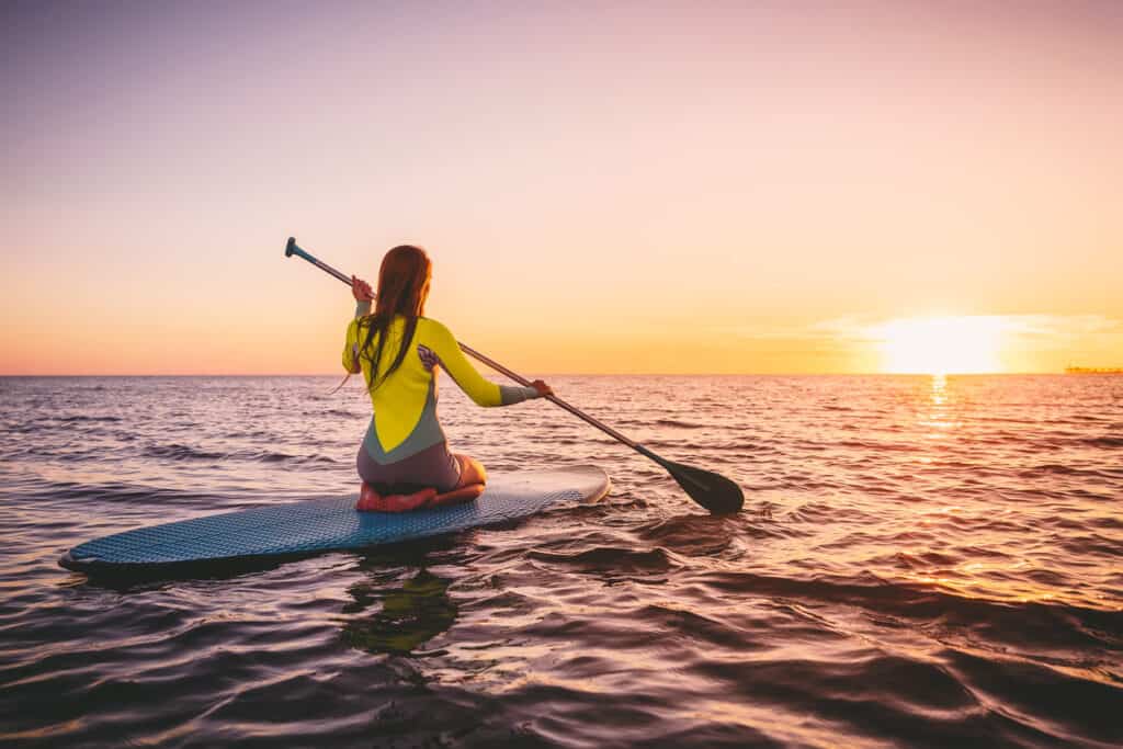 A solo paddleboarder travels out at sunset. Learn about paddleboarding at Boating.Guide.